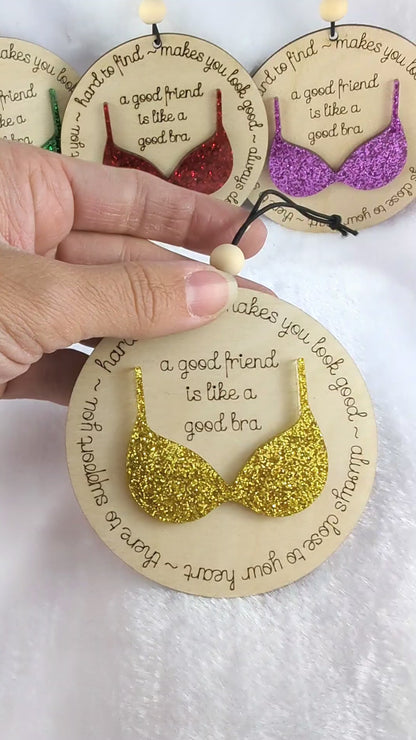 Video of Friendship ornament with a bra. Reads: A good friend is like a good bra. Shows 4 different color options. Red, purple, green and gold glitter bras. 