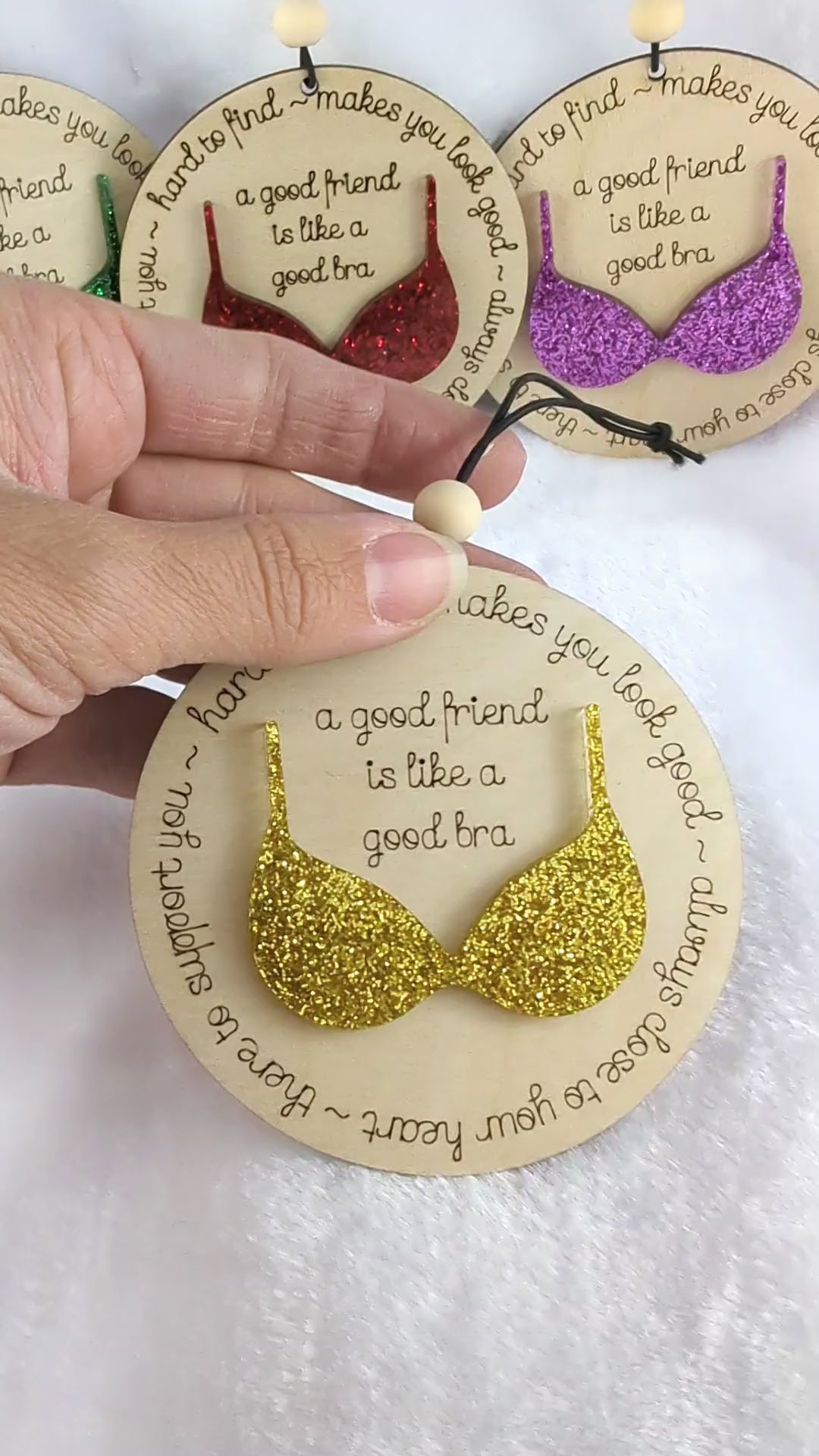 Video of Friendship ornament with a bra. Reads: A good friend is like a good bra. Shows 4 different color options. Red, purple, green and gold glitter bras. 